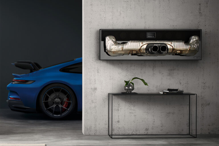 Photo of a blue Porsche 911 behind a cement wall with an exhaust hanging above a glass table