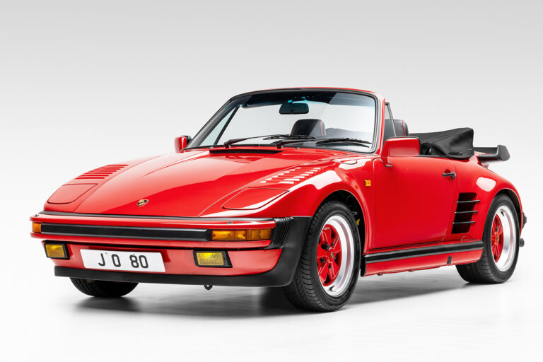 red Porsche 911 turbo cabriolet with black leather top down positioned in a white room