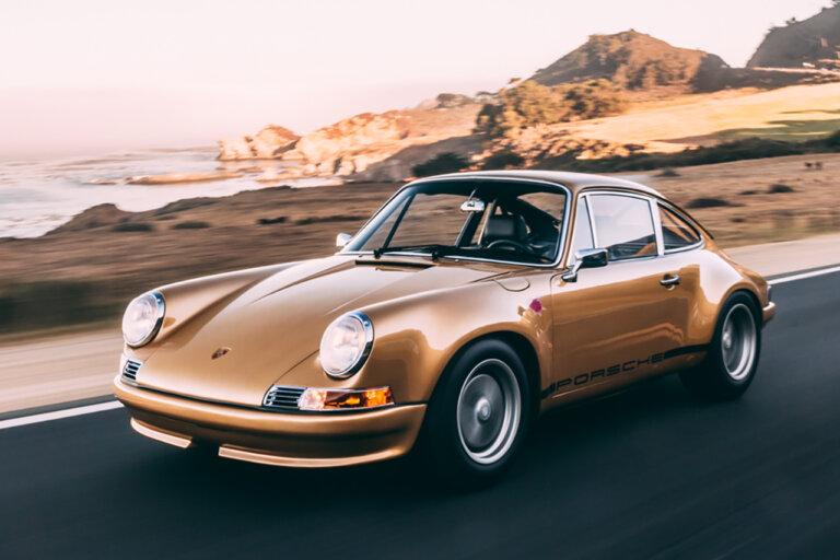 Gold Porsche 911 driving along the coastline with hills in background