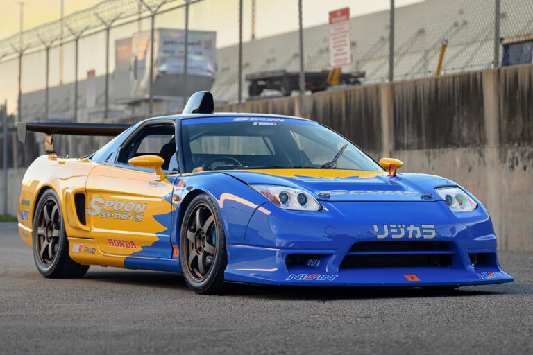 Blue and yellow Honda NSX parked on racetrack with fence in the background
