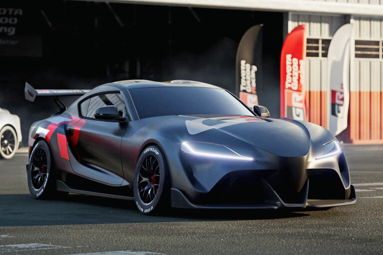 Dark grey Toyota Supra with a large red and white decal towards the rear of the car as the car is staged outside of a garage