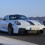 White and black Porsche 911 GT3 driving fast on a racetrack with mountains and blue sky in the background