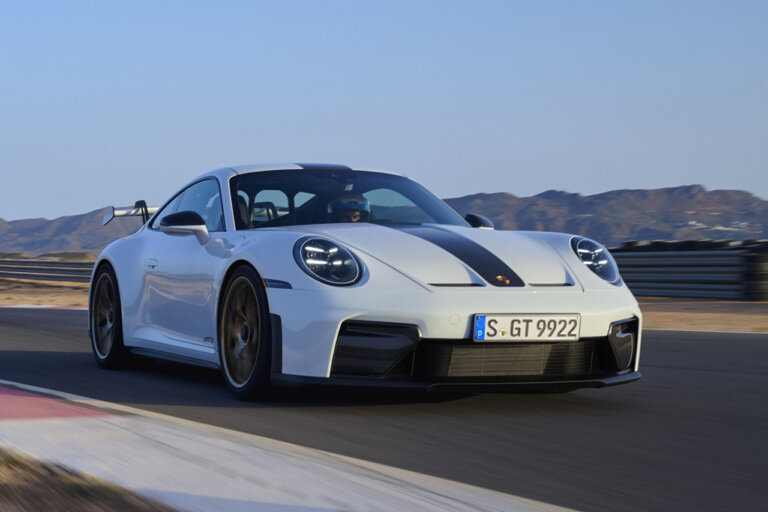 White and black Porsche 911 GT3 driving fast on a racetrack with mountains and blue sky in the background
