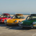 Red, yellow and green Porsche 911's with matching surfboards secured on top of them with the beach coastline in the background