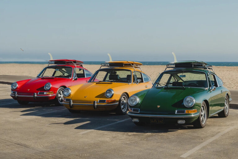 Red, yellow and green Porsche 911's with matching surfboards secured on top of them with the beach coastline in the background
