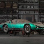 Dirty, dust covered Green Lamborghini propped up on a metal cart in front of shelves holding car parts
