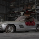Silver with red leather seats of a Mercedes Benz 300 SL parked in a garage with spare parts in the background