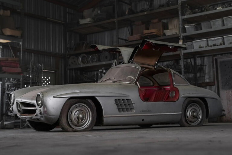 Silver with red leather seats of a Mercedes Benz 300 SL parked in a garage with spare parts in the background