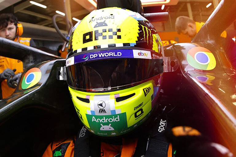 Race car driver with a green helmet covered in stickers strapped down with a Sparco racing harness with people on either side of the driver cockpit
