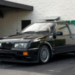 Black Ford Sierra RS500 Cosworth parked in front of a green shrub and white brick wall