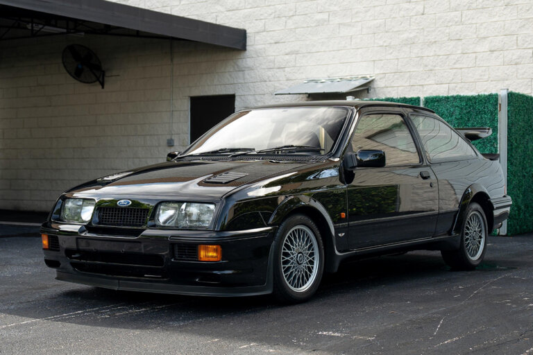 Black Ford Sierra RS500 Cosworth parked in front of a green shrub and white brick wall