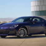 purple Subaru BRZ with chrome wheels parked at an angle in front of a white and blue silo with blue sky in background
