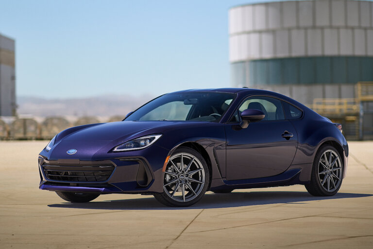 purple Subaru BRZ with chrome wheels parked at an angle in front of a white and blue silo with blue sky in background