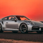Silver Porsche 911 Turbo parked on a road with orange sunset in the background