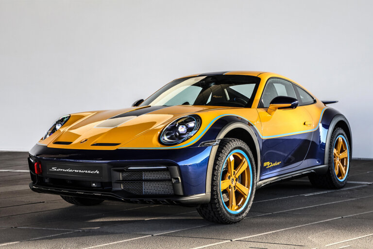 Yellow and blue Porsche 911 Dakar with yellow rims parked in a room with square concrete floor and a white wall.