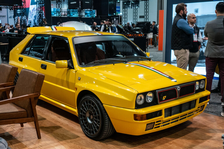Yellow Lancia Delta Evo II parked on wood floor next to leather chairs inside of the SEMA 2024 exhibit