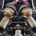 Twin turbo's attached to an engine with straight exhausts pointing out with tubing exposed and wires.