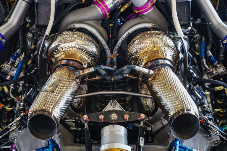Twin turbo's attached to an engine with straight exhausts pointing out with tubing exposed and wires.