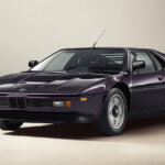 Techno Violet BMW M1 E26 by Ronnie Fieg & KITH shot in front of a beige wall and off white concrete wall.