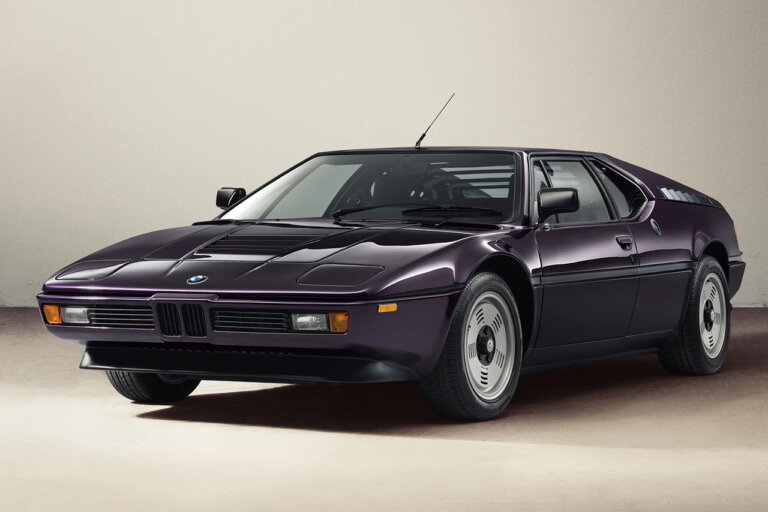 Techno Violet BMW M1 E26 by Ronnie Fieg & KITH shot in front of a beige wall and off white concrete wall.