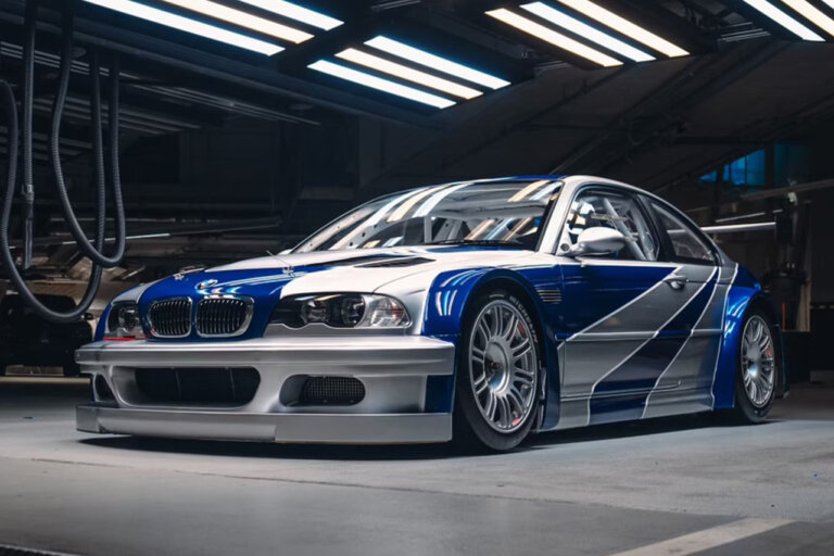 Need For Speed Most Wanted BMW M3 GTR with the silver and blue livery shot in a garage with rows of lights above the car shining down on it.