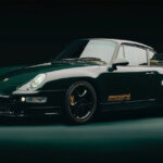 Green Aimé Leon Dore Porsche 993 car pictured in a dark room with a spotlight above the car.