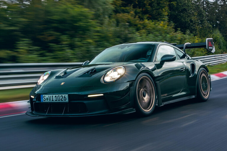 Green Porsche 911 GT3 RS with bronze wheels driving on a racetrack with trees in the background.