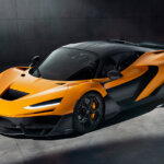 Orange and black McLaren W1 parked in a concrete room with a spotlight pointed at the car with a cast shadow.