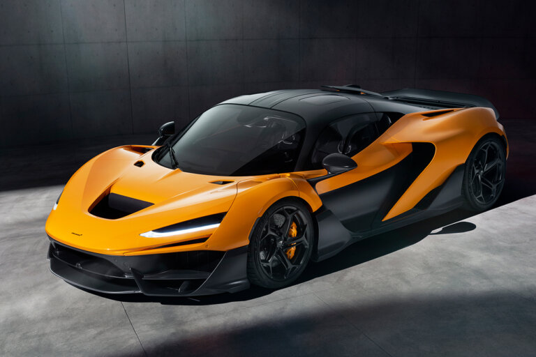 Orange and black McLaren W1 parked in a concrete room with a spotlight pointed at the car with a cast shadow.