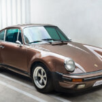 Brown Porsche 911 930 parked in a parking spot with white walls and concrete around the car