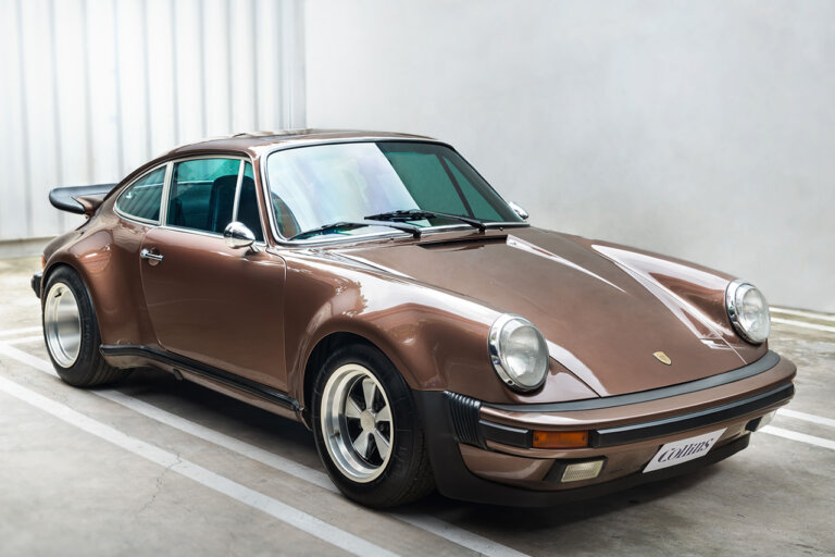 Brown Porsche 911 930 parked in a parking spot with white walls and concrete around the car