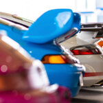 Several Porsche cars all different colors parked next to one another, a purple one out of focus, a blue one, a white one in a showroom floor.